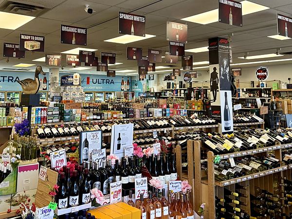 A wide view across the shop floor showing wine tables in the foreground, beer coolers along the back wall and spirits shelving to the right.
