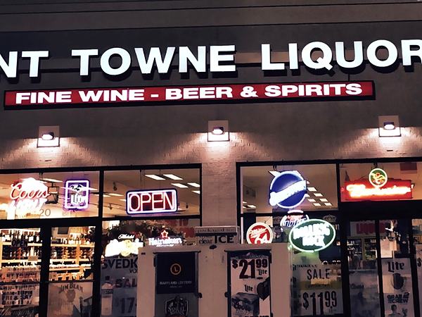 The same shopfront after dark with the sign lit and neon beer signs glowing in the windows.